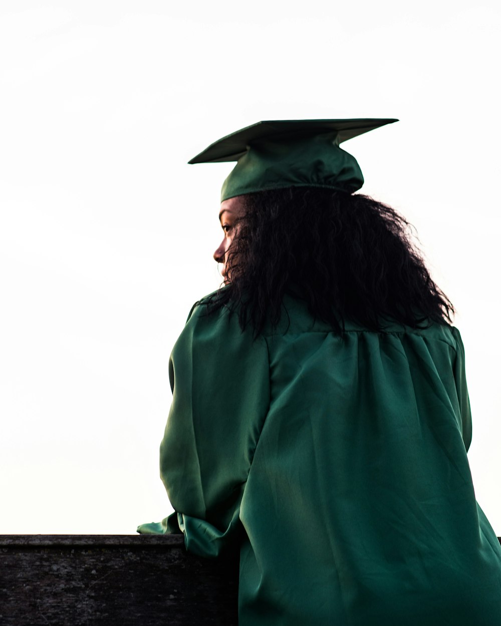 A graduate in a green cap and gown looking out over the horizon