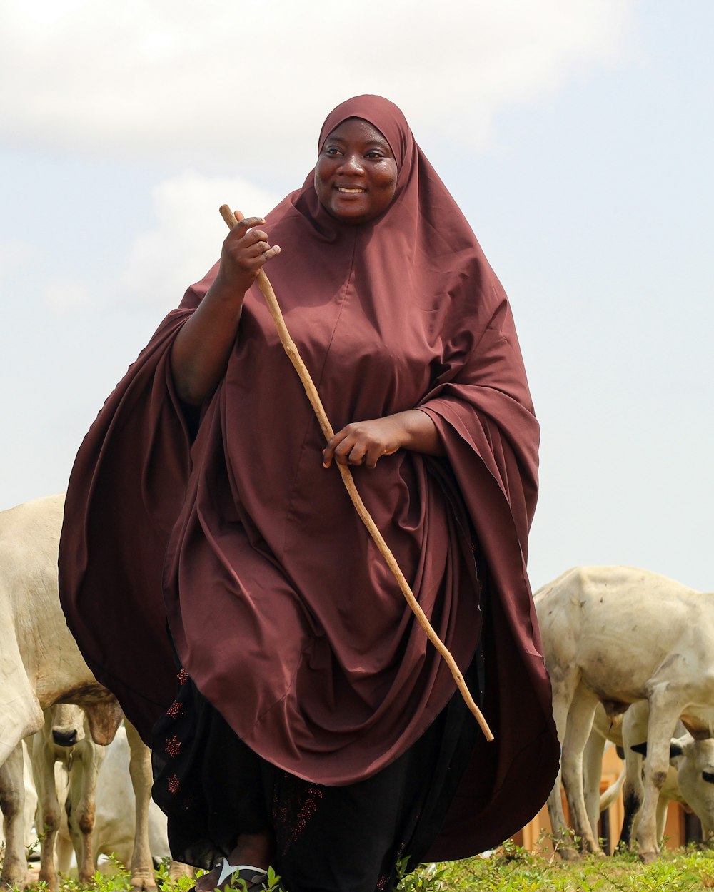 A woman in a deep red robe standing proudly in front of her herd